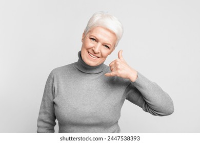 Friendly senior european woman displays a 'call me' hand gesture, suitable for s3niorlife communication themes