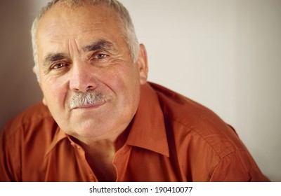 Friendly senior man with a moustache leaning forwards as he looks at the camera with a quiet smile, copyspace on a grey background - Powered by Shutterstock