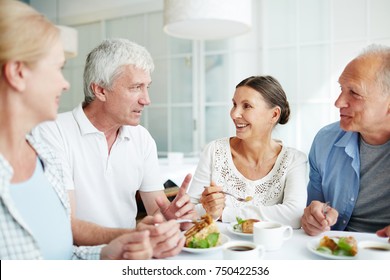 Friendly senior people gathered by table having talk by dessert with tea