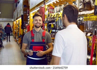 Friendly Shop Assistant At DIY Retail Store Helping Customer Choose Tools And Equipment. Happy Smiling Salesman Helping Young Man Who Is Buying Wrenches And Other Tools For Home Repairs