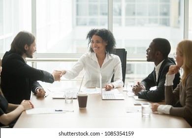 Friendly smiling african businesswoman handshaking caucasian businessman at diverse group meeting, mixed race black female boss welcoming new partner or executive team member shaking hands 
 boardroom