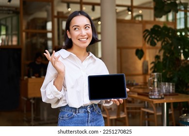 Friendly smiling asian woman, cafe manager, showing tablet screen and looking happy, demonstrating her restaurant profit. - Shutterstock ID 2251270825