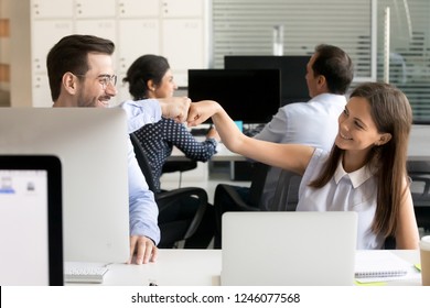 Friendly smiling colleagues fist bumping at workplace, happy coworkers sharing success, young woman and man celebrating good teamwork result, satisfied by collaboration, cooperation at work, respect