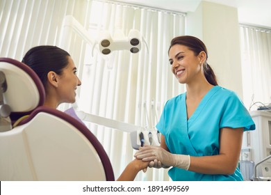 Friendly Smiling Female Dentist In Gloves And Medical Clothes As Sign Of Support Holds Patient Hand Adjusting Her Positive Mood And Asks Not To Worry.