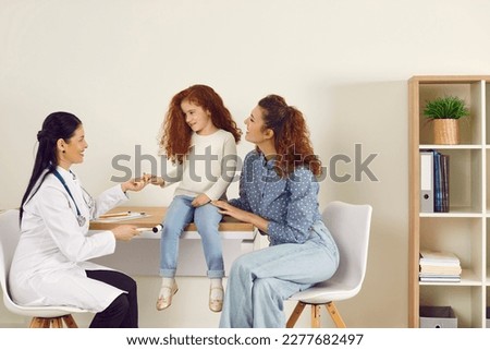 Friendly smiling female doctor examining cute little child. Professional neurologist uses hammer to test knee reflex of happy preschool kid who came to clinic with her mum. Health, neurology concept