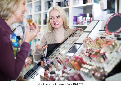 Friendly Smiling Female Seller And Client Near Display With Cosmetics In Beauty Store
