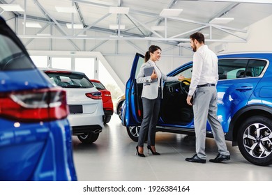 Friendly, smiling female seller showing brand new car to a customer while standing in car salon. - Shutterstock ID 1926384164