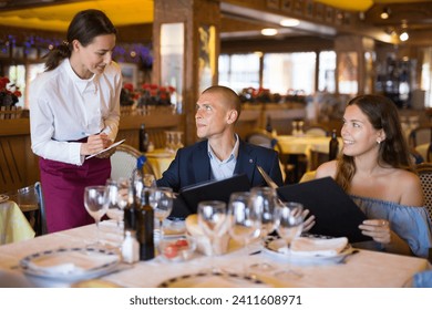 Friendly smiling female waiter consulting couple of guests choosing drinks and meals in restaurant - Powered by Shutterstock