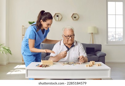 Friendly smiling nurse caregiver in geriatric clinic or retirement home helps senior man with Alzheimer's disease. Happy old man plays puzzles while sitting at table in cozy interior. Dementia concept - Powered by Shutterstock