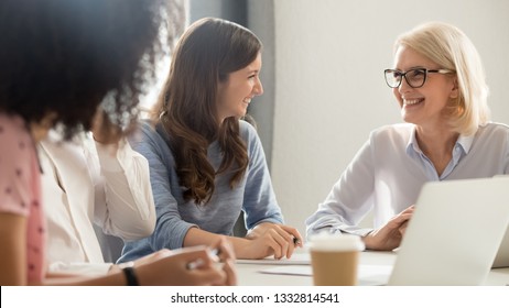 Friendly Smiling Old And Young Businesswomen Talking Laughing At Corporate Group Business Meeting, Happy Female Employees Colleagues Coach Manager And Intern Having Fun Pleasant Conversation At Work