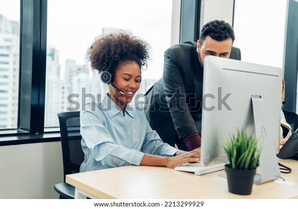 Friendly smiling woman call center operator with\
headset using computer, Customer service, Call center worker\
accompanied by her team at\
office