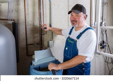 Friendly smiling workman in dungarees installing or working on a water softener in a utility room turning to smile at the camera