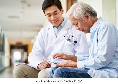 Friendly Smiling Young Asian Doctor Talking And Explaining Test Result To Elderly Patient In Hospital