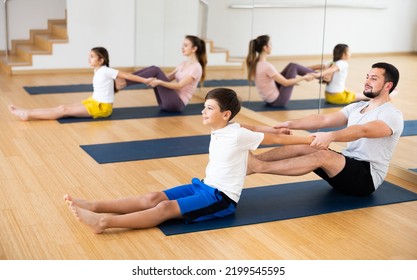 Friendly Sporty Family Practicing Partner Yoga In Fitness Studio. Smiling Tween Boy Doing Exercises On Mat In Pair With His Father