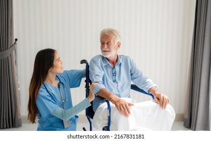 Friendly Staff Caregiver Of Nursing Home Talking To Elderly Man On Wheelchair In The Bedroom.