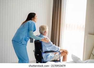 Friendly Staff Caregiver Of Nursing Home Talking To Elderly Man On Wheelchair In The Bedroom.