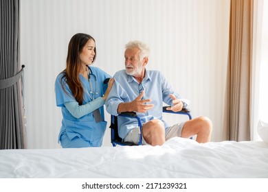 Friendly Staff Caregiver Of Nursing Home Talking To Elderly Man On Wheelchair In The Bedroom.