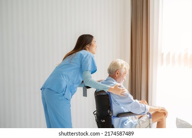 Friendly Staff Caregiver Of Nursing Home Talking To Elderly Man On Wheelchair In The Bedroom.