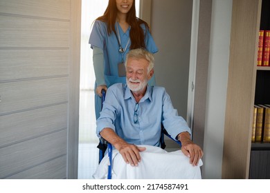 Friendly Staff Caregiver Of Nursing Home Talking To Elderly Man On Wheelchair In The Bedroom.