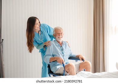 Friendly Staff Caregiver Of Nursing Home Talking To Elderly Man On Wheelchair In The Bedroom.