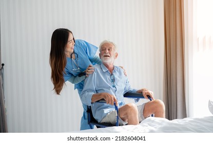 Friendly Staff Caregiver Of Nursing Home Talking To Elderly Man On Wheelchair In The Bedroom.