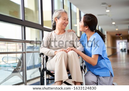 friendly staff caregiver of nursing home talking to asian senior woman in hallway