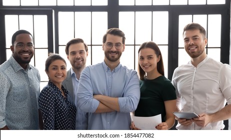 Friendly Team. Group Portrait Of Successful Multiethnic Business Team In Office, Confident Charismatic Man Leader Posing Indoors Surrounded By Happy Diverse Staff Members Smiling And Looking At Camera