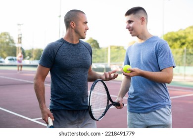 Friendly teenage boy and adult man chatting on outdoor tennis court. - Powered by Shutterstock