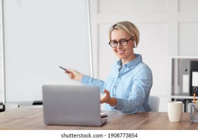 Friendly University Tutor Teaching Remote School Class, Giving Online Lesson On Laptop, Pointing At Empty Blackboard With Copy Space. College Professor Conducting Webinar Or Conference