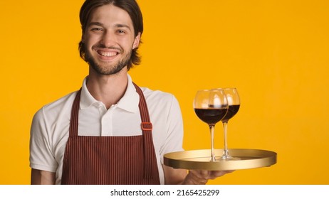 Friendly waiter holding tray with wine glasses over colorful background. Young bearded man in apron smiling at camera isolated - Powered by Shutterstock