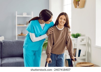 Friendly woman doctor, nurse or caregiver in uniform helps happy child patient girl with broken leg walk with orthopedic crutches at home. Injury, rehabilitation concept - Powered by Shutterstock