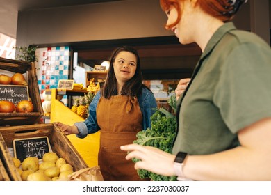 Friendly woman with Down syndrome assisting a customer in the vegetable section of a grocery store. Professional woman with an intellectual disability working as a store assistant in a supermarket. - Powered by Shutterstock