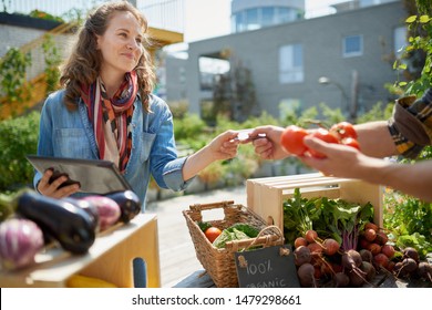Friendly woman tending an organic vegetable stall at a farmer's market and selling fresh vegetables from the rooftop garden