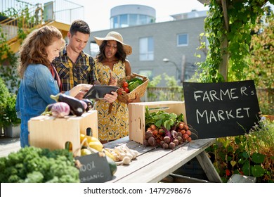 Friendly woman tending an organic vegetable stall at a farmer's market and selling fresh vegetables from the rooftop garden - Powered by Shutterstock