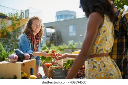 Friendly woman tending an organic vegetable stall at a farmer's market and selling fresh vegetables from the rooftop garden - Powered by Shutterstock