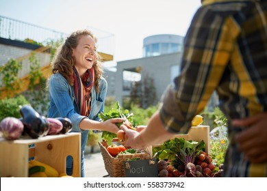 Venlig kvinde, der har en økologisk grøntsagsstall på en landmands marked og sælger friske grøntsager fra taghaven