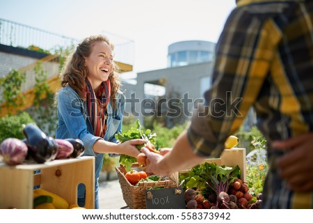 Friendly woman tending an organic vegetable stall at a farmer's market and selling fresh vegetables from the rooftop garden