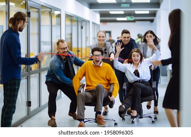 Friendly Work Team  Ride Chairs In Office Room Cheerfully Excited Diverse Employees Laugh While Enjoying Fun Work Break Activities, Creative Friendly Workers Play A Game Together.