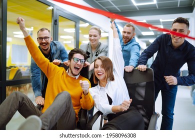 Friendly Work Team  Ride Chairs In Office Room Cheerfully Excited Diverse Employees Laugh While Enjoying Fun Work Break Activities, Creative Friendly Workers Play A Game Together.