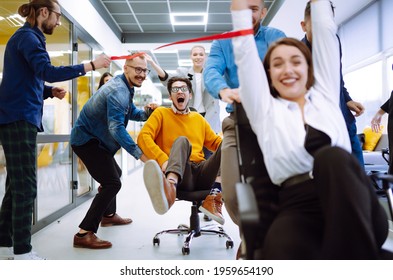 Friendly Work Team  Ride Chairs In Office Room Cheerfully Excited Diverse Employees Laugh While Enjoying Fun Work Break Activities, Creative Friendly Workers Play A Game Together.