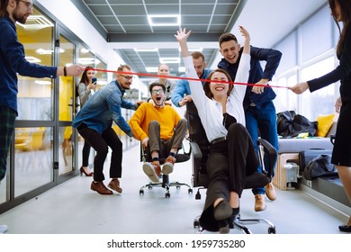 Friendly Work Team  Ride Chairs In Office Room Cheerfully Excited Diverse Employees Laugh While Enjoying Fun Work Break Activities, Creative Friendly Workers Play A Game Together.