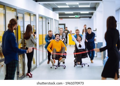 Friendly Work Team  Ride Chairs In Office Room Cheerfully Excited Diverse Employees Laugh While Enjoying Fun Work Break Activities, Creative Friendly Workers Play A Game Together.