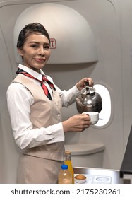 Friendly young Asian cabin crew serving coffee on plane, female flight attendant preparing food and drink for passengers on board,airhostess working on plane, smiling airline worker holding coffee cup