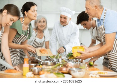 Friendly young Asian woman holding cutting board with fresh salmon steak and talking to elderly man during group culinary classes.. - Powered by Shutterstock