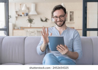 Friendly young caucasian man freelancer having video call zoom on digital tablet pad, communicating with relatives, girlfriend, doctor, friends, workers employees online at home. Remote work concept - Powered by Shutterstock