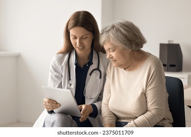 Friendly young female therapist in uniform show medical health checkup results on digital tablet to senior woman, explain prescription or treatment plan, discuss therapy in clinic. Elderly healthcare - Powered by Shutterstock