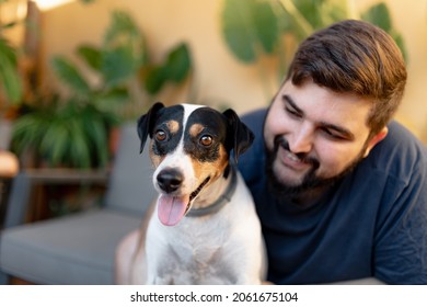 Friendly Young Man Hugging His Cute Grocer Dog With Both Hands While Looking At Him, The Dog Has The Tongue Out While Looking At Camera