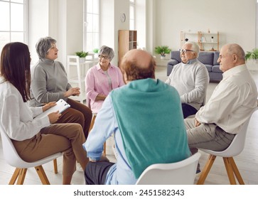 Friendly young nurse, caregiver or psychologist woman having conversation with a group of senior people men and women sitting in a circle. Psychological support for retirement people in nursing home. - Powered by Shutterstock