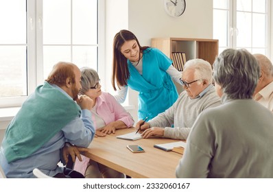 Friendly young nurse woman having conversation with a group of senior people men and women sitting at the table. Leisure and caregiver support for retirement people in nursing home. - Powered by Shutterstock