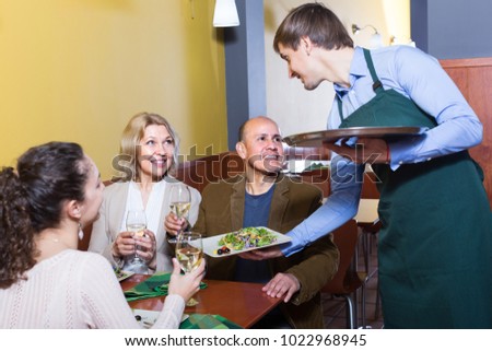Friendly  young waiter serving table with happy adults in restaurant 